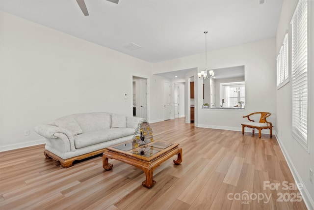 living room with light wood-type flooring and ceiling fan with notable chandelier