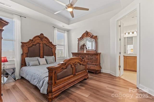 bedroom featuring connected bathroom, ceiling fan, a tray ceiling, and light hardwood / wood-style flooring