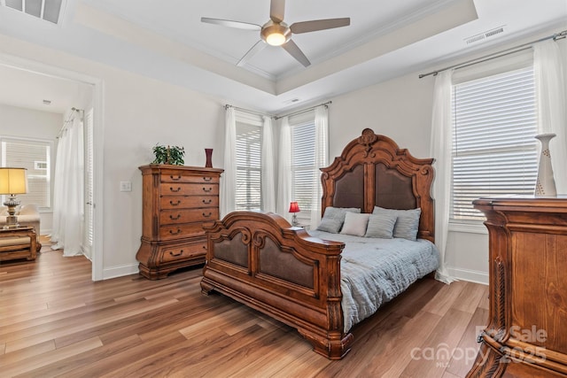 bedroom with ceiling fan, multiple windows, a raised ceiling, and hardwood / wood-style flooring