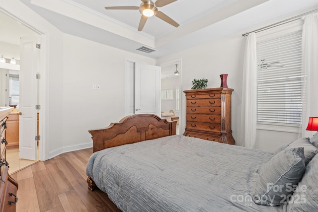 bedroom featuring ensuite bathroom, a raised ceiling, ceiling fan, light wood-type flooring, and crown molding