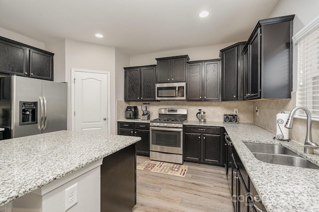 kitchen featuring tasteful backsplash, light stone counters, stainless steel appliances, sink, and light hardwood / wood-style floors