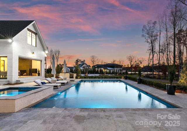 pool at dusk featuring a patio and an in ground hot tub