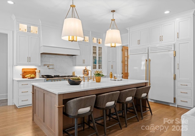 kitchen with stainless steel gas stovetop, a center island with sink, white cabinets, and decorative light fixtures