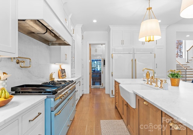 kitchen with high end appliances, white cabinets, light stone counters, and decorative light fixtures