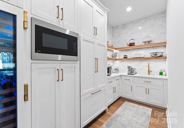 interior space featuring built in microwave, wine cooler, sink, light hardwood / wood-style flooring, and white cabinets