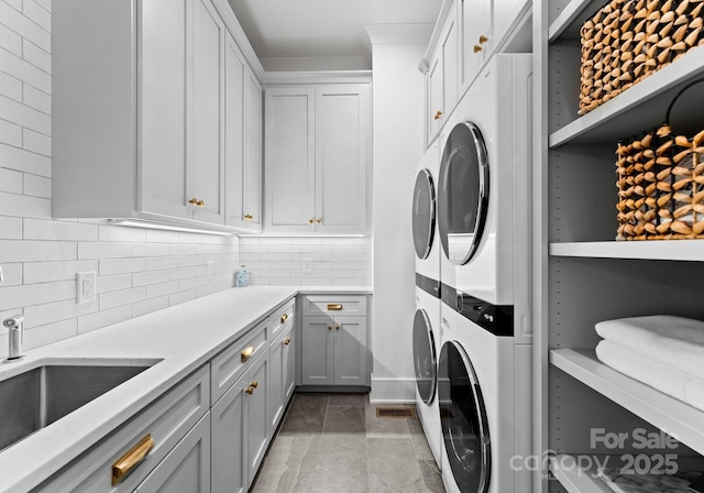 clothes washing area with sink, cabinets, and stacked washing maching and dryer