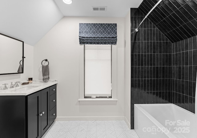 bathroom with tiled shower / bath, vaulted ceiling, and vanity