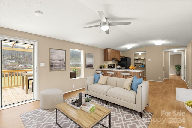 living room featuring ceiling fan, lofted ceiling, a textured ceiling, and light hardwood / wood-style flooring