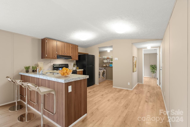 kitchen featuring kitchen peninsula, light wood-type flooring, sink, washer and dryer, and black appliances