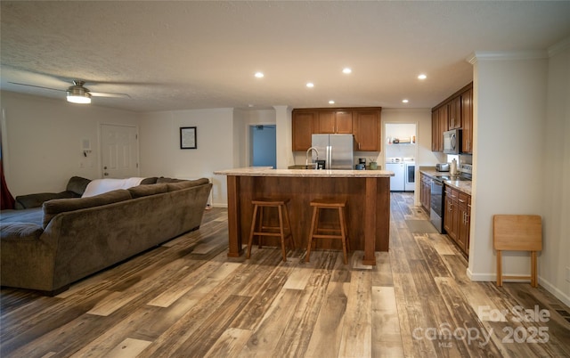 kitchen with dark wood-type flooring, separate washer and dryer, a kitchen island with sink, a breakfast bar, and appliances with stainless steel finishes