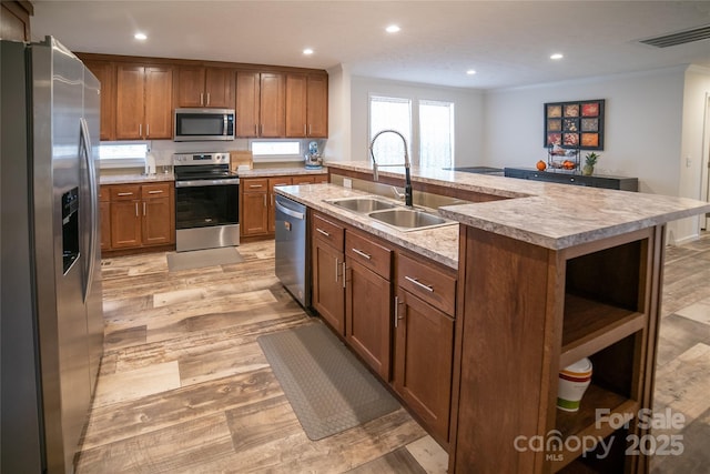 kitchen featuring sink, stainless steel appliances, crown molding, light hardwood / wood-style floors, and a kitchen island with sink