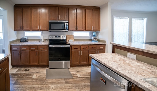 kitchen featuring ornamental molding, appliances with stainless steel finishes, and light hardwood / wood-style flooring