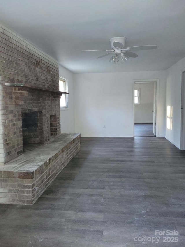 unfurnished living room with a brick fireplace, ceiling fan, and dark wood-type flooring