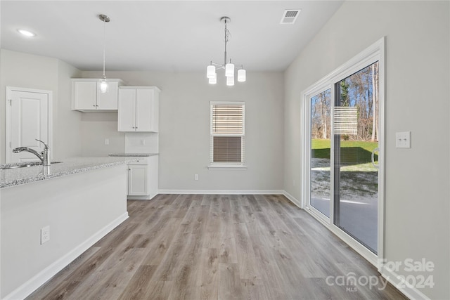 kitchen featuring hanging light fixtures, white cabinetry, sink, and light stone counters