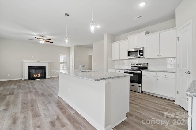 kitchen with hanging light fixtures, white cabinetry, a center island with sink, and stainless steel appliances