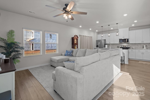 living room with ceiling fan, sink, and light wood-type flooring