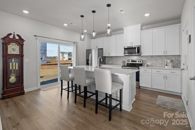 kitchen featuring pendant lighting, a center island with sink, white cabinets, and stainless steel appliances