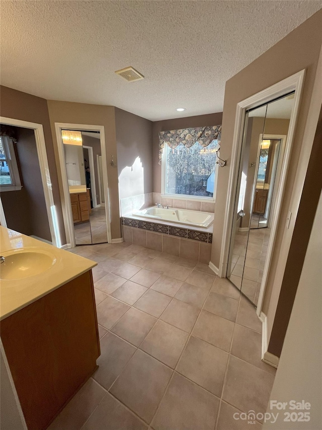 bathroom with tile patterned flooring, a textured ceiling, vanity, and a relaxing tiled tub