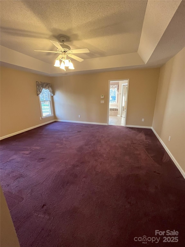 spare room with dark carpet, a textured ceiling, a raised ceiling, and ceiling fan