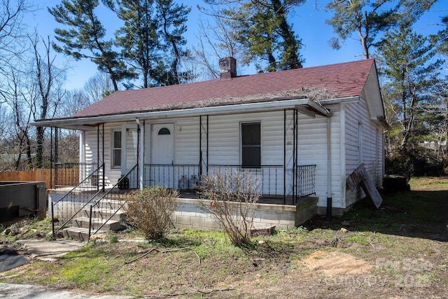 view of front of house with roof with shingles, a porch, and a chimney