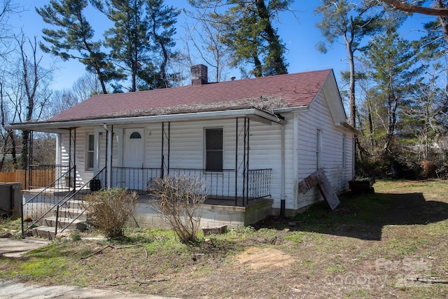 view of front of home with a porch, a chimney, and roof with shingles