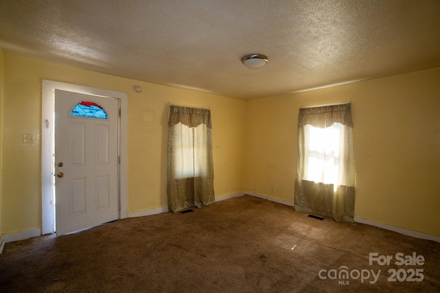 carpeted foyer entrance with visible vents, baseboards, and a textured ceiling