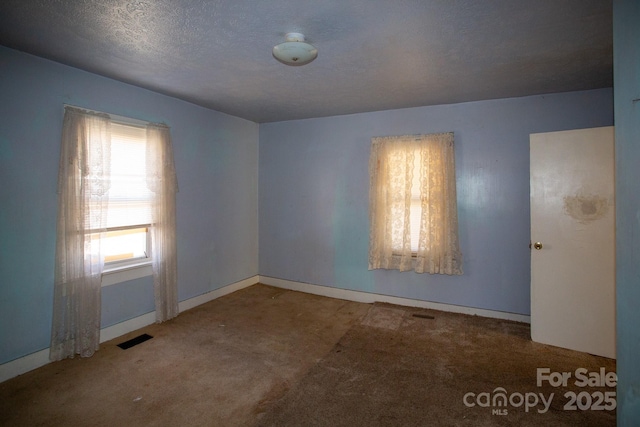 unfurnished room with visible vents, a textured ceiling, and carpet