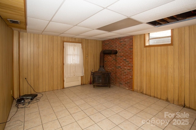 basement featuring a drop ceiling, wooden walls, and a wood stove