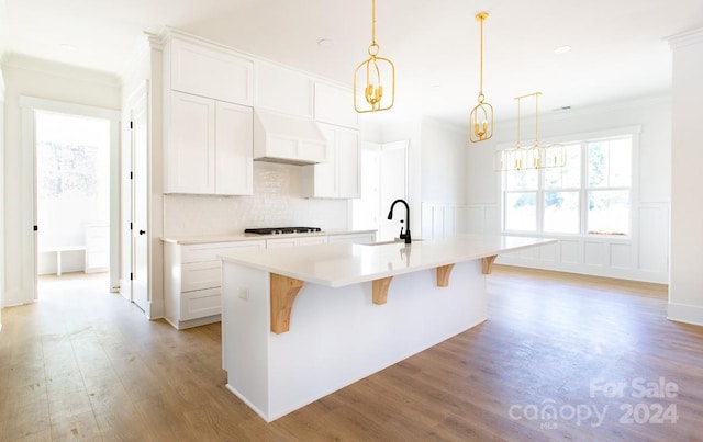 kitchen with white cabinetry, sink, hanging light fixtures, premium range hood, and a kitchen island with sink