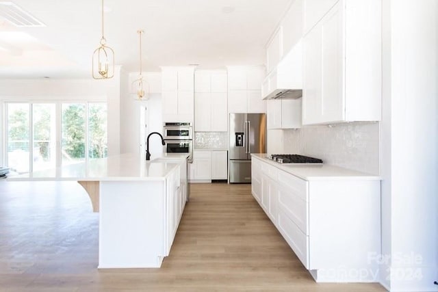 kitchen with tasteful backsplash, an island with sink, decorative light fixtures, white cabinets, and appliances with stainless steel finishes