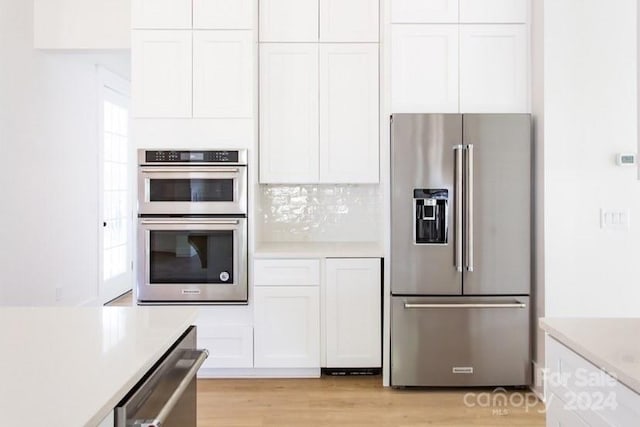 kitchen with white cabinets, stainless steel appliances, light hardwood / wood-style flooring, and tasteful backsplash