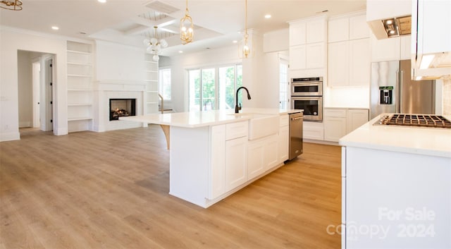 kitchen with sink, an island with sink, appliances with stainless steel finishes, decorative light fixtures, and white cabinetry