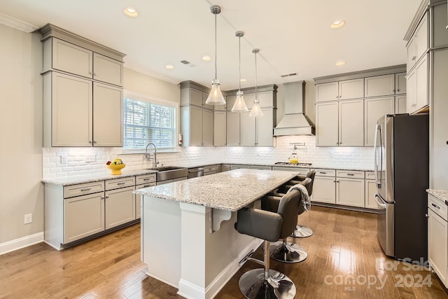 kitchen with appliances with stainless steel finishes, light stone counters, custom exhaust hood, a center island, and a breakfast bar area