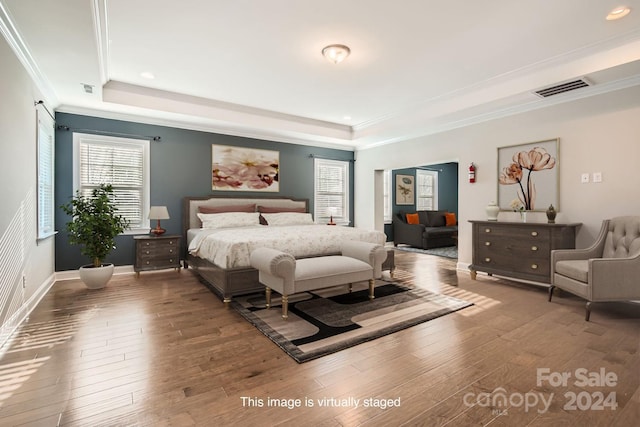 bedroom with wood-type flooring, a raised ceiling, and ornamental molding