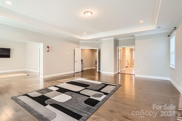 empty room with a raised ceiling, dark wood-type flooring, and crown molding