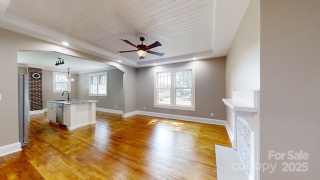 unfurnished living room featuring sink, wooden ceiling, light hardwood / wood-style flooring, a tray ceiling, and ceiling fan with notable chandelier