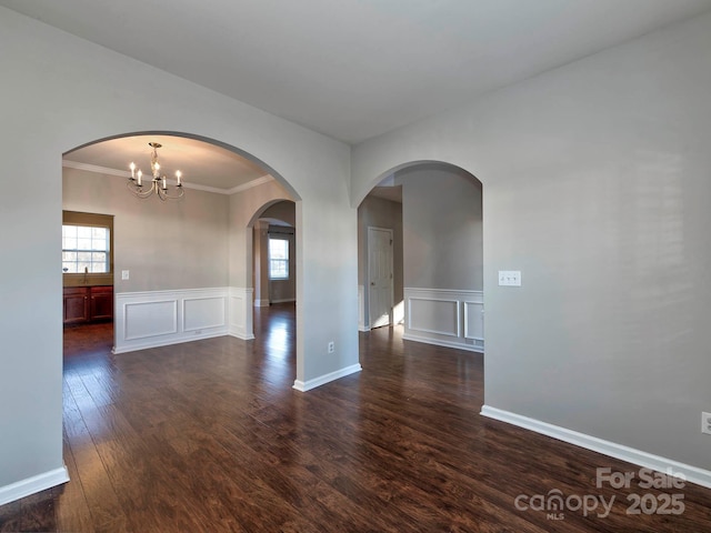 spare room with dark wood-type flooring, crown molding, a wealth of natural light, and a notable chandelier