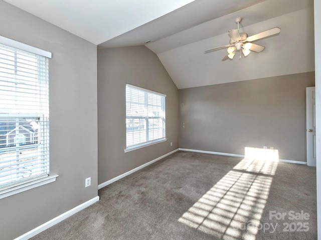 spare room with dark colored carpet, lofted ceiling, ceiling fan, and a healthy amount of sunlight