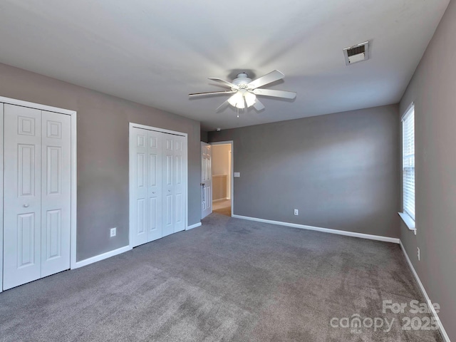 unfurnished bedroom with dark colored carpet, ceiling fan, and multiple closets