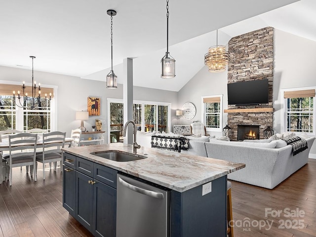 kitchen with light stone counters, stainless steel dishwasher, a kitchen island with sink, sink, and decorative light fixtures