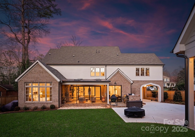 back house at dusk featuring a fire pit, a sunroom, a patio, and a lawn