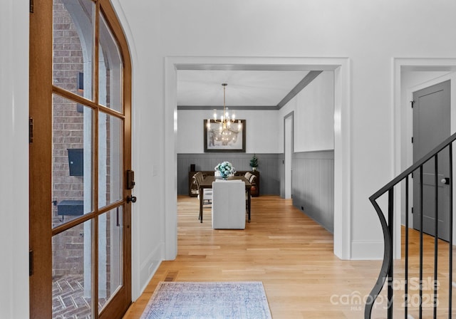 foyer entrance featuring stairway, a wainscoted wall, an inviting chandelier, ornamental molding, and light wood-style floors