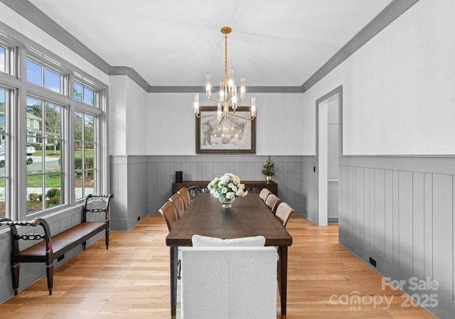 dining area featuring ornamental molding, light wood-style floors, a chandelier, and wainscoting