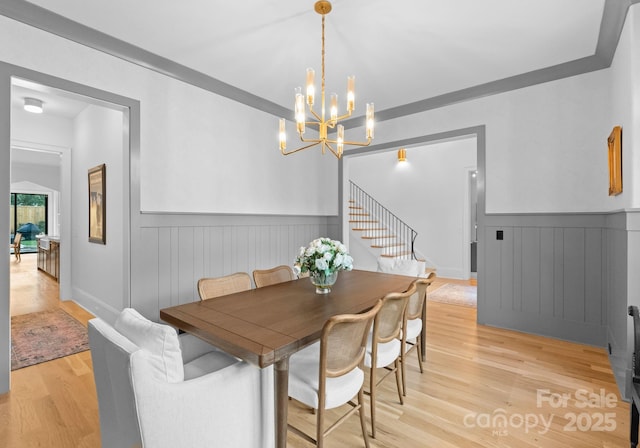 dining room with stairs, light wood-style flooring, a notable chandelier, and wainscoting