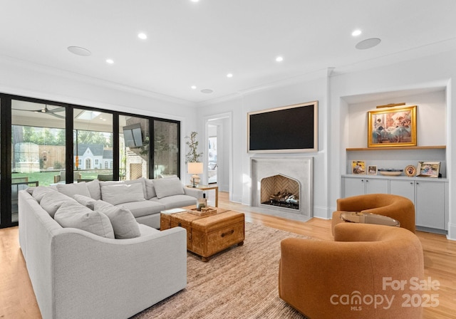 living room featuring a fireplace with flush hearth, recessed lighting, light wood finished floors, and ornamental molding