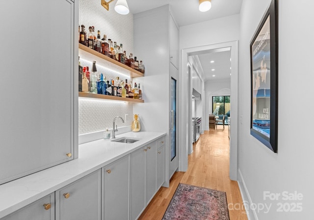 bar featuring light stone countertops, decorative backsplash, sink, light hardwood / wood-style flooring, and gray cabinets