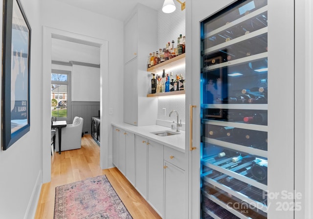 bar featuring beverage cooler, a wainscoted wall, light wood finished floors, a sink, and indoor wet bar