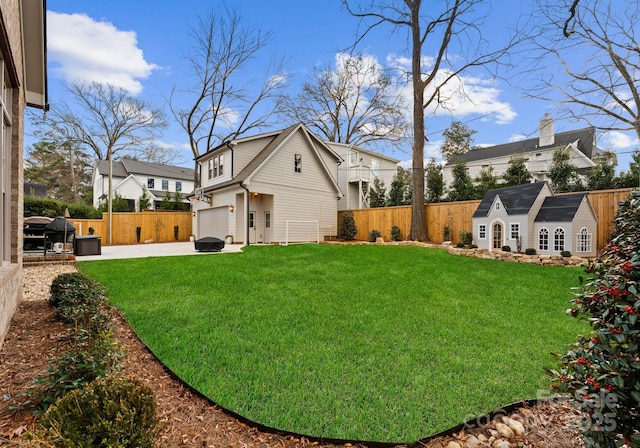 view of yard with an outbuilding, driveway, a patio, a fenced backyard, and an attached garage