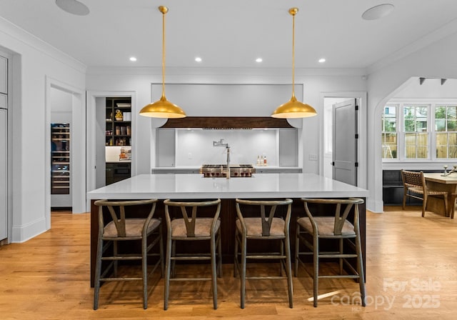 kitchen featuring light hardwood / wood-style floors, ornamental molding, hanging light fixtures, and a large island with sink