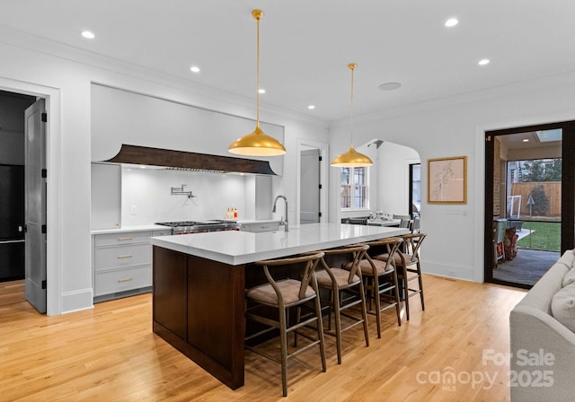 kitchen with light wood finished floors, a breakfast bar, arched walkways, ornamental molding, and light countertops